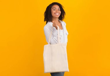 Plastik Kirliliği Durdur. Sarı arka planda beyaz çantalı mutlu Afrikalı kız, taklit et.