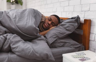 Hasta siyah adam evde soğuk algınlığı ve grip belirtileri göstererek yatakta yatıyor. Yatak odasında dinlenen Afrika kökenli Amerikalı adam Coronavirüs hastalığından muzdarip. Covid-19 Konsepti. Seçici Odaklanma