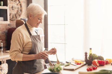Sağlıklı beslenmenin faydaları. Pozitif kıdemli bayan mutfakta taze salata pişirme, boş alan