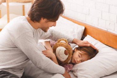 Uyan, güzelim. Baba, uyuyan küçük kızını uyandırıyor. Kız, oyuncak ayıyı kucaklıyor. Evin içinde.