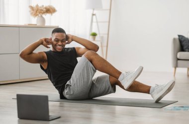 Antrenman yapıyorum. Diz dirseğe antrenman yapan mutlu siyahi adam dizüstü bilgisayarda egzersiz yapıyor evde online antrenman izliyor. Spor adam oturma odasında karın kaslarını kasıyor.