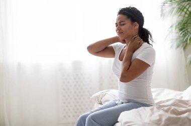 Rahatsız edici yatak. Siyah adam boynu ağrıyan bir şekilde uyanıyor, genç Afrikalı Amerikalı kadın evde oturmuş kaşlarını çatıyor ve masaj yapıyor, boşluğu kopyalıyor.