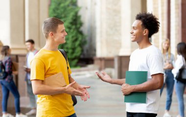 Neşeli öğrenciler dışarıda bir şeyler tartışıyor, üniversite kampüsünde mola veriyorlar.