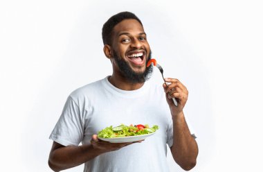 Akşam yemeğinde sağlıklı salata yiyen mutlu Afrikalı Amerikalı adam stüdyoda beyaz arka planda poz veriyor. Erkek Kilo Verme, Beslenme Konsepti. Siyahi adam sebze yemeğinin tadını çıkarıyor.