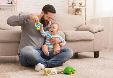 Kopya alanı parlak rattle, evde, katta oturan bebek oğluyla oynamaktan mutlu baba