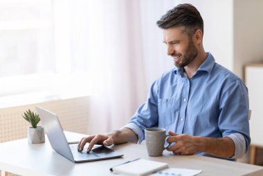 İçişleri Bakanlığı. Gülümseyen Freelancer Laptop 'ta e-postaları kontrol ediyor, kahve içiyor, uzaktan çalışmanın keyfini çıkarıyor, Boşluğu kopyalıyor.