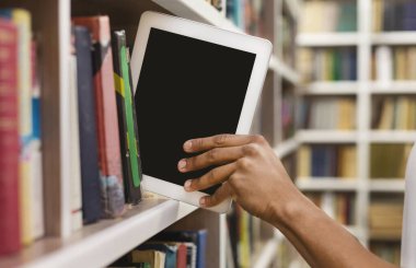 Modern teknolojiler ve bilgi. Kütüphanede rafta boş ekranlı dijital tablet koyan öğrenci, boş alan