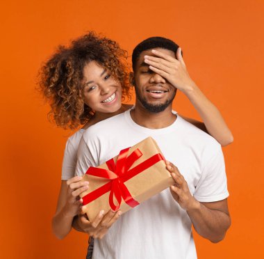 Gizli hediye. Şirin Afrikalı kız, erkek arkadaşının gözlerini kapatıyor ve ona mevcut, turuncu stüdyo geçmişi veriyor.