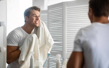 Günlük rutin konsept. Modern banyoda dururken yüzünü havluyla silen yakışıklı bir adam.