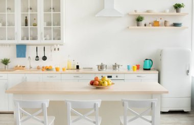 Sağlıklı yiyecekler, vitaminler, modern dairenin iç tasarımı. Masadaki renkli elmalar, çaydanlık ve beyaz mobilyaların üzerindeki parlak bardaklar ve sabahları tabakları boş olan yemek odası.