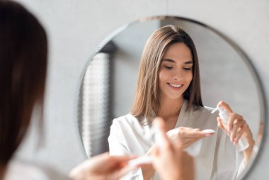 Banyoda aynanın yanında dururken pamuk pedde temizlik jeli süren çekici genç bayan yüz derisinden makyajı çıkaran güzel bir kadın, yansımaya odaklanıyor.