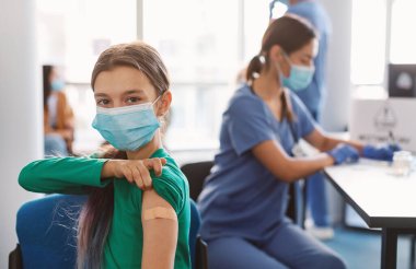 Kapalı Aşılama Konsepti. Cerrahi Maskeli Mutlu Ergen Kız Corona Virüs Aşısını klinikten aldıktan sonra koluna yapıştırıcı bandaj yapıştırıyor. Antiviral Enjeksiyon