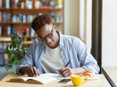 Çalışkan siyah adam ders kitabından bilgi yazıyor, kafede test için hazırlanıyor. Kafede okuyan havalı Afrikalı Amerikalı çocuk ödevi için veri topluyor, ev ödevi yapıyor.