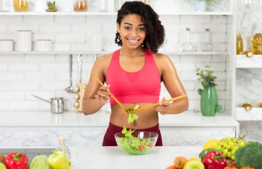 Vejetaryen Konsepti. Mutfağın içinde sağlıklı süper yemek salatası pişiren afro kadın, malzemeleri karıştırıyor.