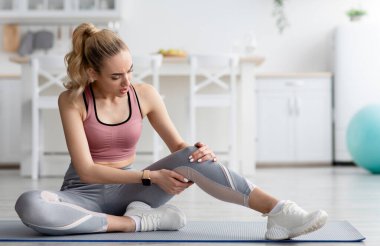 Evde antrenman sakatlığı. Kadın evde egzersiz yaptıktan sonra acı çekiyor. Diz ağrısı çeken, spor giyim sektöründeki umutsuz sarışın kadın minimalist oturma odasında, mutfağın içinde, fotokopi odasında.