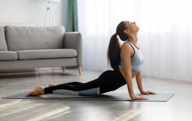 Spor kıyafetli esnek genç bir kadın evde yoga yapıyor oturma odasında yoga minderinin üzerine uzanıyor ve vücudunu, yan bakışını, kopyalama alanını esnetiyor. Yoga pozu, ev konseptinde yoga pratiği.