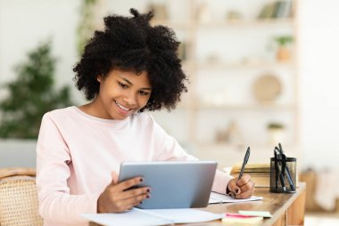 Dijital tablet kullanan mutlu genç kız evde ders çalışıyor. Çevrimiçi Eğitim, E-Öğrenme Konsepti. Seçici Odaklanma