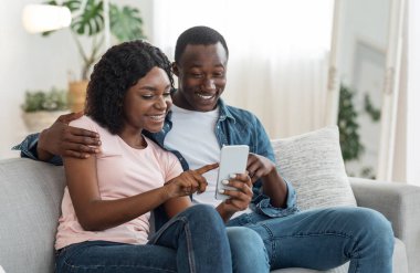 Heyecanlı siyah çift yeni mobil uygulamayı kontrol ediyor, ev içi, kopyalama alanı