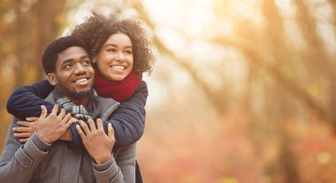 Sonbahar eğlencesi ve aşk konsepti. Parkta yürüyen aşık bir çift, bir adam bir kadına sırtına biniyor, boş bir alan.