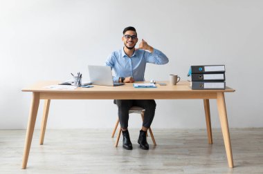 Beni geri ara. Gözlüklü genç, gülümseyen bir Arap, elinde bilgisayarla el hareketleriyle kameraya bakarak işaret işareti yapıyor. İletişim ve Cep Hücresel Bağlantı Kavramı