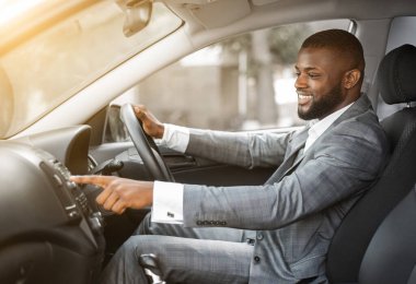 Takım elbiseli Afrikalı Amerikalı adam hareket etmeden önce arabada müzik açıyor. Neşeli siyah işadamı arabasındaki fonksiyonel panele basıyor, iş gezisine başlamadan önce müziği açıyor.