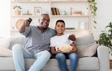 Mutlu siyah dedesi ve torunu kanepede oturup patlamış mısır yiyor ve evde birlikte televizyon izliyorlar.