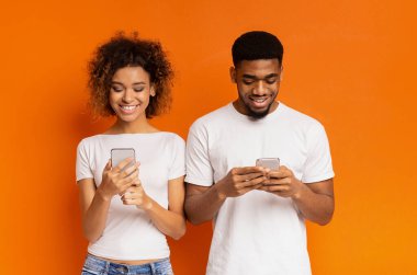 Siyah bin yıllık çift ağ veya arkadaş, turuncu arka plan ile sohbet cep telefonları üzerinde tarama