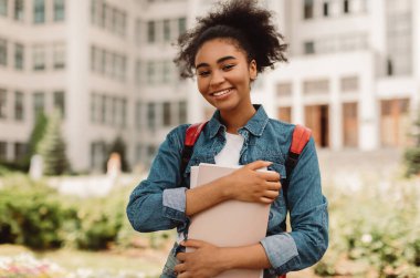 Başarılı Öğrencinin Portresi. Dışarıda modern üniversite binasının yanında duran kameraya gülümseyen mutlu Afrikalı Amerikalı genç kız poz veriyor. Öğrencilik, Modern Eğitim