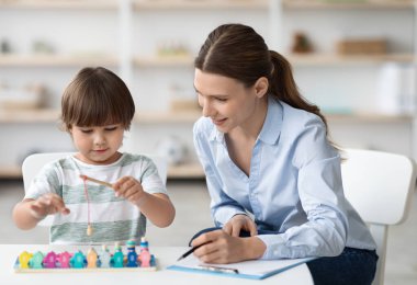 Erken gelişim kavramı. Psikolojik seans sırasında ahşap balıkçılık oyunlarıyla oynayan mutlu küçük çocuk dikkatli kadın uzmanlar ofiste notlar alıyor.
