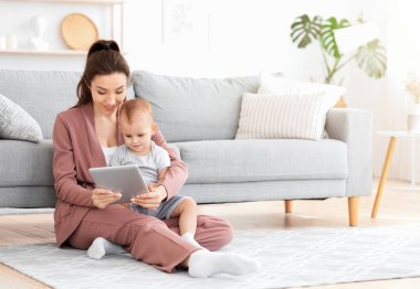 Gülümseyen anne ve sevimli oğlu evde dijital tablette çizgi film izliyorlar oturma odasında yerde oturuyorlar.