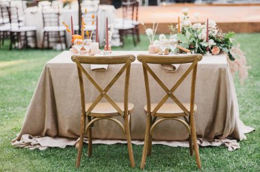 Kırsal düğün seti, süsleri, çiçekleri, boho stili, etkinliği, partisi ya da düğünü olan klasik yemek masası. Ahşap sandalyeler, keten masa örtüsü, mumlar, aksesuarlar ve bardaklar çimenlikteki yeni evli masasında.