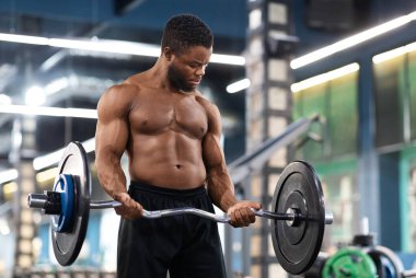Atletik siyah adam ağırlık kaldırıyor, ağırlık kaldırıyor, kol ve göğüs kasları üzerinde çalışıyor, fotokopi çekiyor. Modern spor salonunda ağır halterlerle egzersiz yapan kaslı Afrikalı Amerikalı vücut geliştirici.