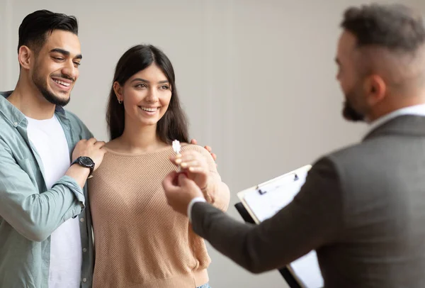 Mutlu gülümseyen Orta Doğulu çift gelecekteki yeni dairenin anahtarını alıyor. Takım elbiseli profesyonel bir emlakçı genç alıcılara anahtar veriyor. İpotek, Satılık Mülkiyet