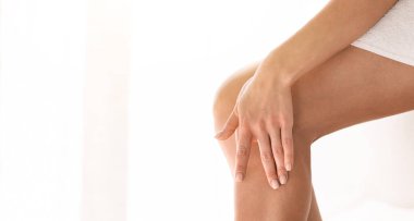 Kusursuz bir cilt, yumuşak dokunuş, epilasyon ve epilasyon. Mükemmel cilde sahip genç bir kadın, bacağa elle dokunur, banyoda, beyaz pencere zemininde, kırpılmış.