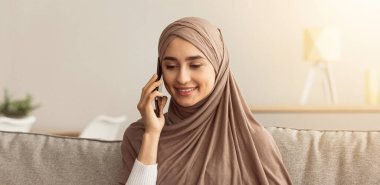 Modern online iş kumandası, güvenli ve covid-19 salgını sırasında yeni normal olun. Tesettürlü, tesettürlü genç bir Arap kadın beyaz bir müşteriyle konuşuyor ve oturma odasında dizüstü bilgisayar kullanıyor, boş alan.