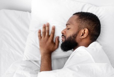 Sakin, sakallı, beyaz yatakta, yatak odasındaki yorganın altında yumuşak yastıkta uyuyan Afro-Amerikan bir adam. Sağlıklı bir uyku çeken, geceleri, hafta sonları ya da tatillerde dinlenen bir adam.