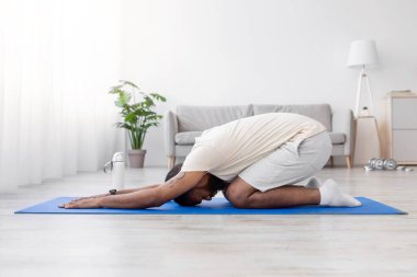 Sakallı, beyaz spor giyim giymiş, oturma odasının iç tarafında yoga yapan sakin, Afro-Amerikan bir erkek. Spor ve sağlıklı yaşam tarzı, sabahları spor, fotokopi alanı