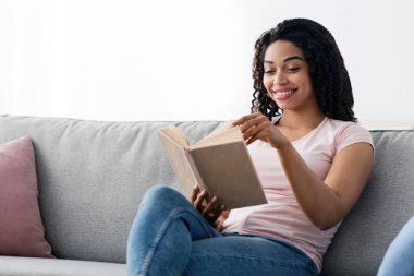 Günlük, not defteri, hobiler ve edebiyat ile evde bir gün planla. İçeride dinlen ve rahatla. Minimum oturma odasında kitap ya da günlük okuyan mutlu Afro-Amerikan kadın. İç mekan boş.