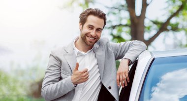 Mükemmel kalitede bir araba, onay, otomobil blogu ve galeride çalışma. Modern yeni ulaşım aracının yanında kirli sakallı, neşeli, beyaz bir adam, baş parmağını gösteriyor, satın almayı onaylıyor, açık havada