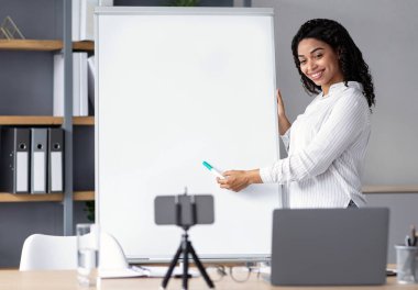 Çevrimiçi ve yeni normaller için İngilizce dersi veren öğretmen. Mutlu şirin Afro-Amerikan kadınları kara tahtayı gösterip aletin webcam 'ine bakar ve evdeki öğrenciler için video çeker.