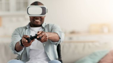 Afrika kökenli Amerikalı milenyum adamı oturma odasında rahatlıyor, oyun oynuyor, oyun sahası kullanıyor. Neşeli orta yaşlı adam tekerlekli sandalyede ve video gözlüklü oyun kumandalı bilgisayar, kopyalama alanı