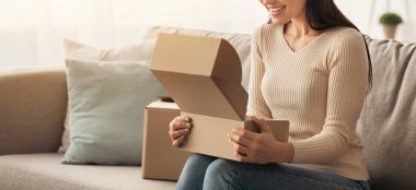 Memnun müşteri çevrimiçi sipariş aldı, hızlı teslimat hizmeti. Bin yıllık heyecanlı Arap dişisi karton kutuları satın alarak açıyor, minimalist oturma odasındaki kanepede oturuyor.