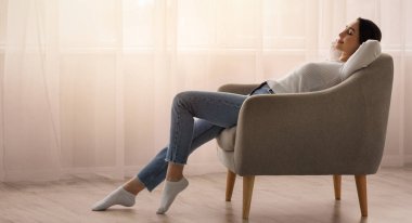 Boş zamanlarınızda evde dinlenin, işten ve hafta sonundan uzaklaşın. Mutlu, barışçıl, çekici Arap kadın pencere arkasında, oturma odasında, iç mekanda, profilde, kopyalama alanında oturuyor.