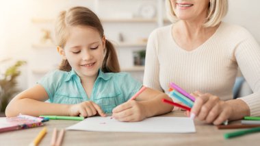 Kreş etkinliği, bebek bakıcılığı konsepti. Mutlu olgun bir kadın masasında oturmuş, sevimli bir anaokulu kızıyla kağıt albüm çizmekten zevk alıyor, Coloful kalemleri kullanıyor.