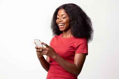 Arkadaşlarıyla mesajlaşmak için akıllı telefon kullanan neşeli siyahi kadının portresi, Beyaz Stüdyo Arkaplanı 'nın başında dikilirken cep telefonuyla mesajlaşan mutlu Afrikalı Amerikalı bayan,