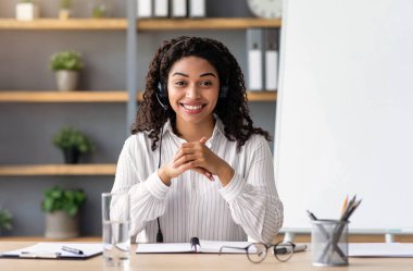 Öğrencilerle yakınlaştırma konferansı, evde online ders, öğretmenle modern eğitim, covid-19 salgını. Kara tahtada kulaklık takmış, web kamerasına bakan gülümseyen Afro-Amerikan kadın.