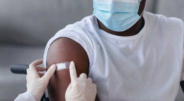 Engellilerin sağlığıyla ilgilenmek, risk grubunun aşılanması, aşılama ve tıbbi hizmetler. Eldivenli doktor koruyucu maskeli siyahi hastaya iğne yaptıktan sonra sıva uygular.