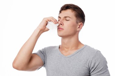 Hüzünlü, genç, beyaz, yakışıklı adam peçeteyi burun buruna bastırıyor ve beyaz arka planda izole bir şekilde kanaması ya da burnu akıyor. Yaralanma, yüksek tansiyon, sağlık sorunları, nezle ve grip