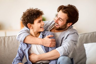 İki kuşak kavramı. Mutlu baba oğlunu kucaklıyor, birbirine bakıyor ve gülümsüyor, evdeki kanepede oturuyor. Aile birlikte zaman geçirmek, boş alan.