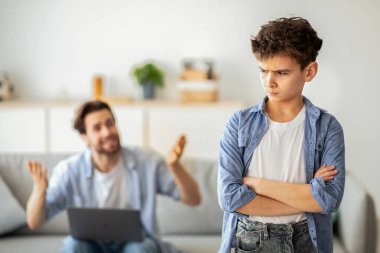 Öfkeli genç baba, evdeki koltukta dizüstü bilgisayarla otururken oğluna bağırıyor, seçici bir şekilde. Aile sorunları, yanlış anlama kavramı